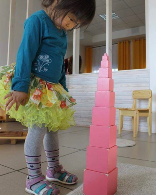 . Montessori student walking along the extended Pink Tower on the floor, exploring size gradation and balance in a sensorial activity.