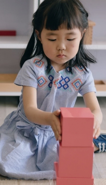 Young girl engaging with the Montessori Pink Tower, developing focus and coordination through hands-on learning in a Montessori classroom.